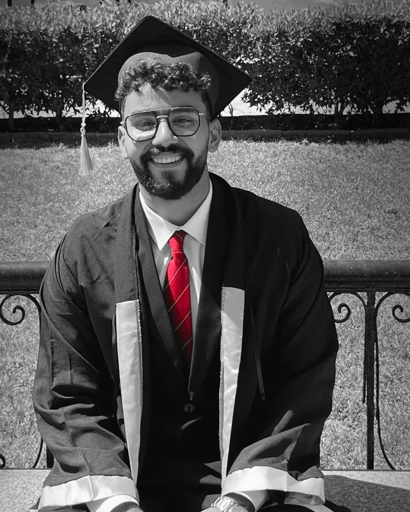 Mahmoud Elsallal at his graduation, in a black gown and cap, smiling — black-and-white except for his red tie